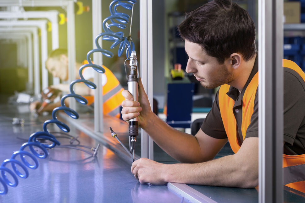 Worker using a precision electric screwdriver with cable support system on an industrial assembly line for controlled screwing process