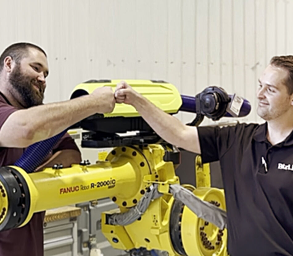 Two employees of R.A.B. Industries and BizLink Robotic Solutions shaking hands on top of a Fanuc robot