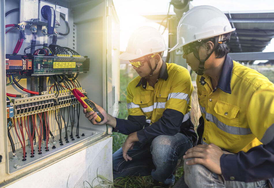 Two workers with white helmets and yellow warn vests checking on open fuse cabinet